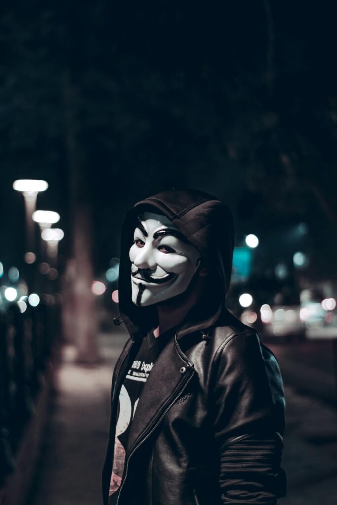 pexels-photo-1863170-1863170 A person wearing a Guy Fawkes mask poses on a dimly lit urban street at night.