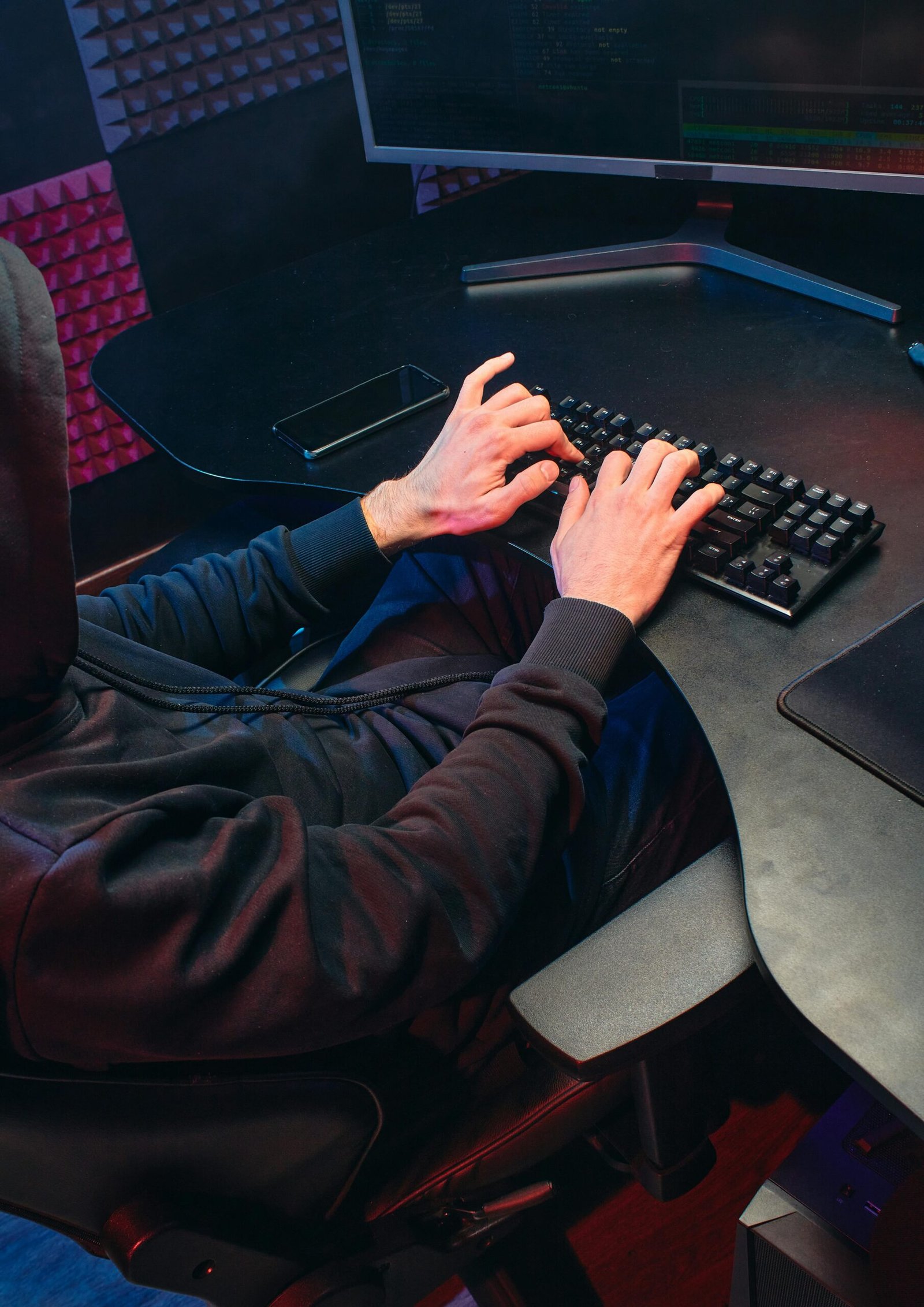 pexels-photo-6964348-6964348 Person in hoodie typing on a keyboard in a dark room, focusing on hacking activities.
